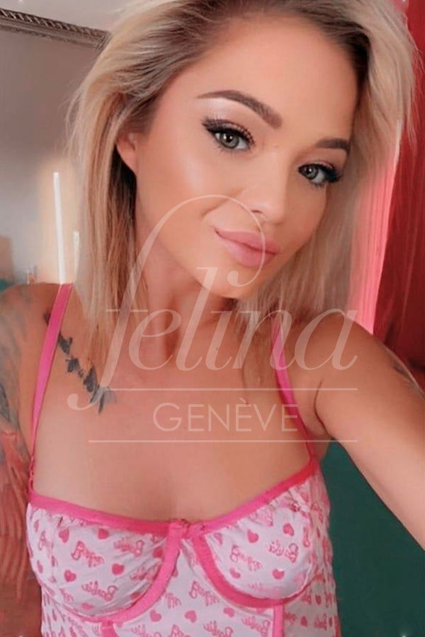 Escort rubia de ojos azules, tatuada, tomándose un selfie